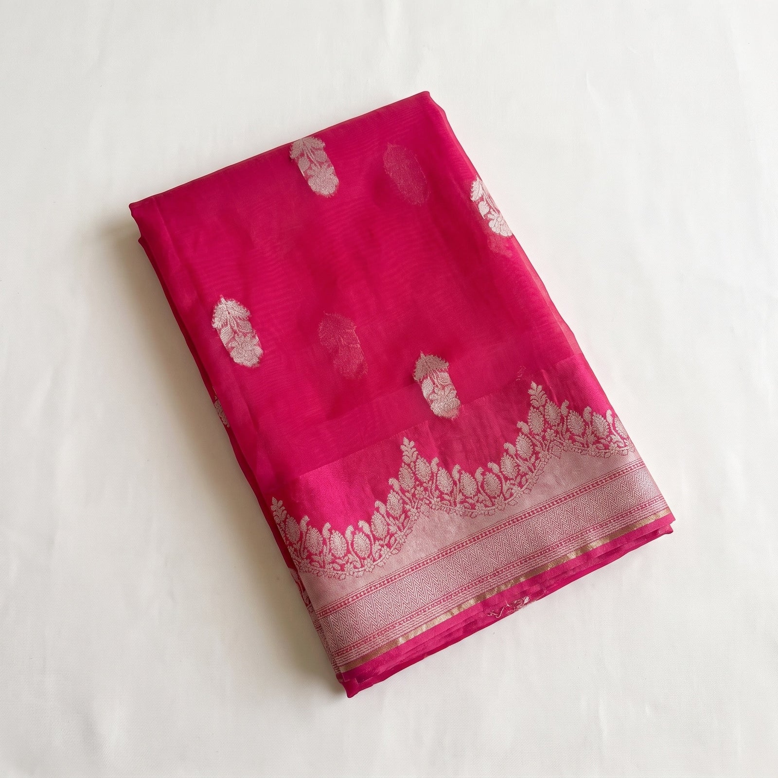 Folded pink pure kora organza saree showing woven motifs and border