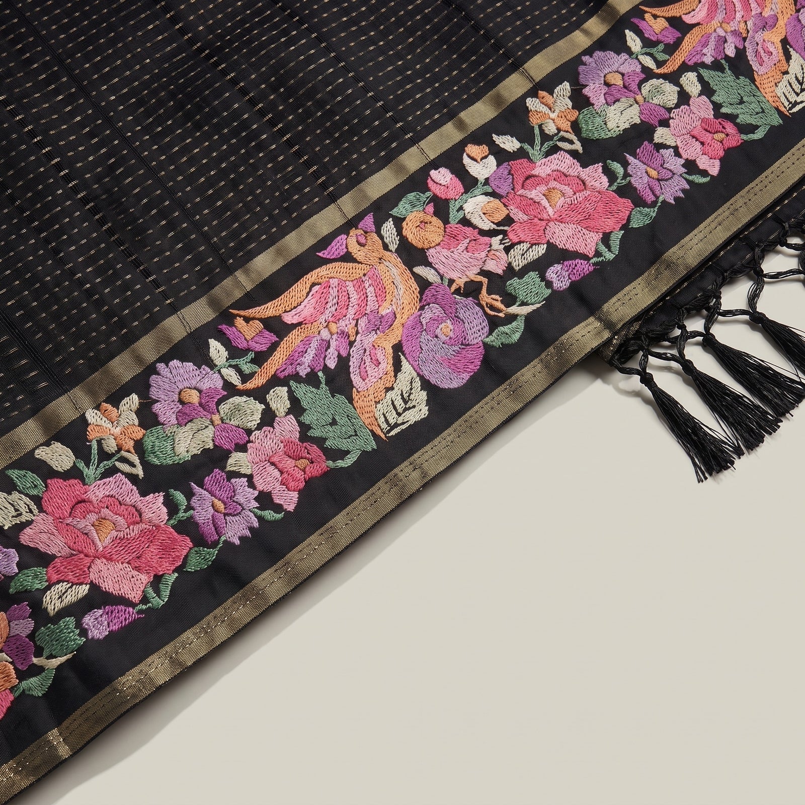Folded view of black pure tussar saree showcasing embroidered border and tassels